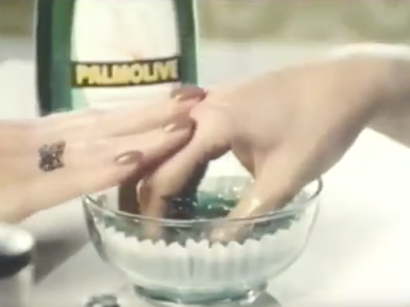 Still from Palmolive ad depicting woman with hand in a bowl of palmolive.