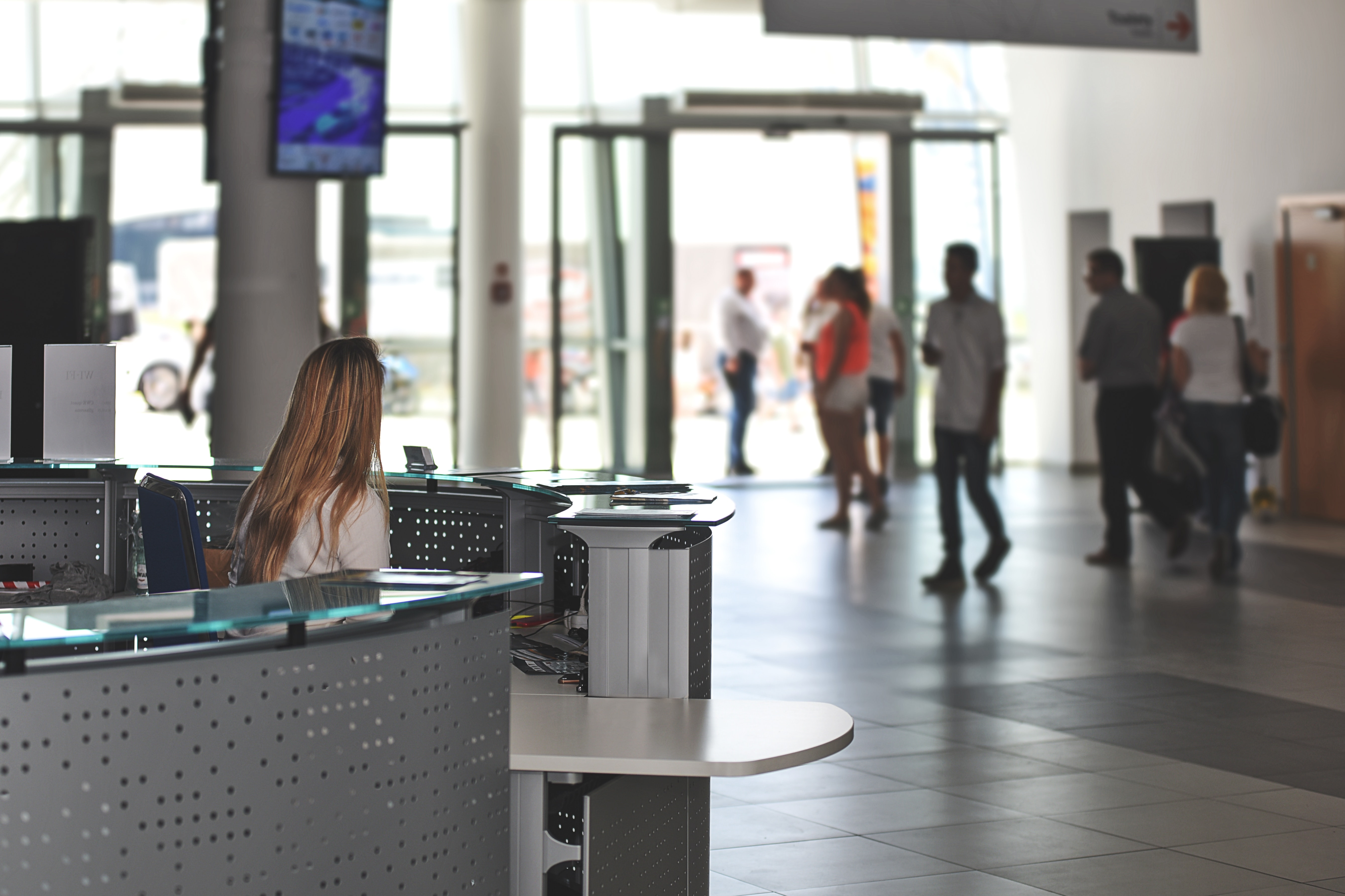 Photo showing woman at large desk with customers in the distance. Customer relationship management software isn't always exciting but it is necessary for many businesses. 